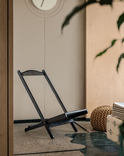 Black folding chair with corded seat in a wood-paneled corner beside a round clock