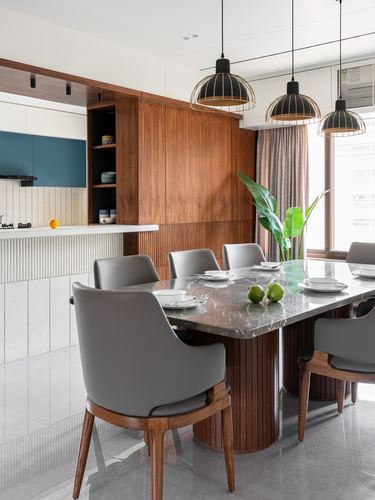 Dining table with grey chairs under three black cage pendant lights, wood cabinetry behind