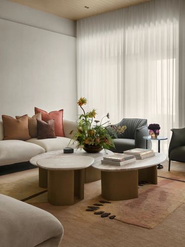Living room with cream sectional, fluted marble coffee tables, sheer curtains and terracotta cushions
