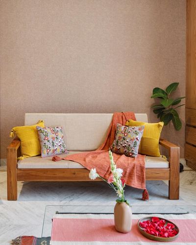 Wooden sofa with mustard and floral cushions against a beige textured wall, styled with flowers