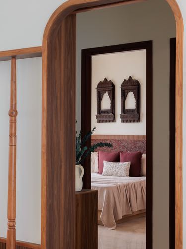View through a curved wooden archway into a bedroom with carved wall niches and a maroon headboard