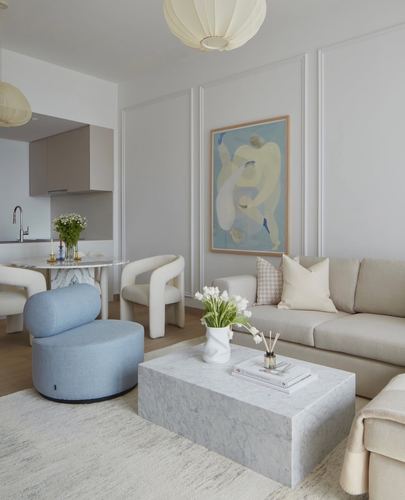Neutral living room with marble coffee table, cream sofa, blue bouclé ottoman and figurative wall art