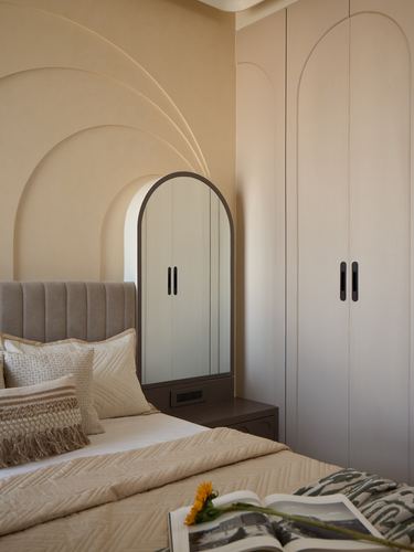 Beige bedroom corner with arched wall panelling, arched mirror, and tufted headboard