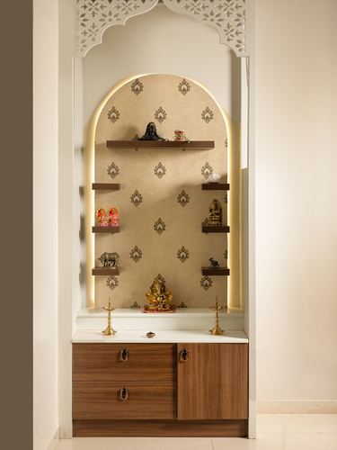 Arched pooja unit with patterned backdrop, floating shelves holding idols, and wooden cabinet below