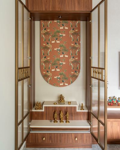 Wooden pooja unit with brass idols and an arched patterned panel behind them