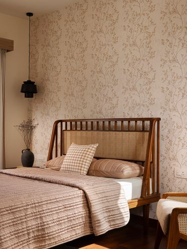 Bed with cane and wood headboard against floral wallpaper, black pendant light beside bedside vase