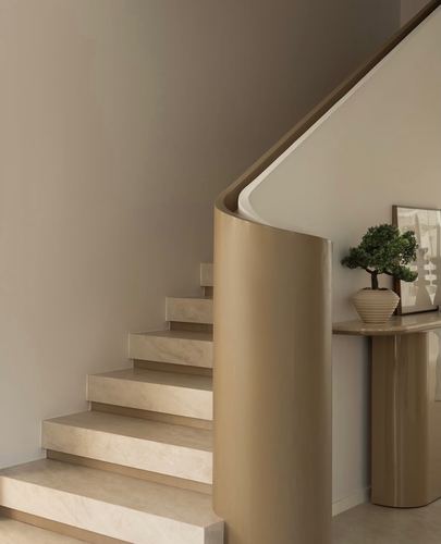 Curved bronze staircase balustrade beside a matching console table with plant and artwork