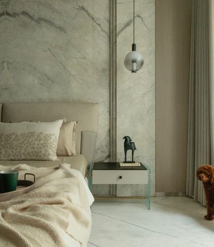 Bedroom corner with marble-look wall, glass nightstand, globe pendant light, and small dog by curtain