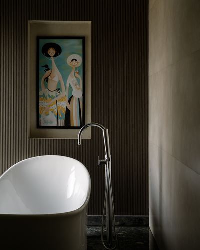 Freestanding white tub with chrome floor filler beneath a framed artwork niche in dark ribbed wall.