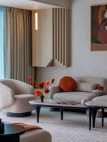Beige living room with boucle sofa, ribbed wood wall feature, marble coffee tables, red flowers