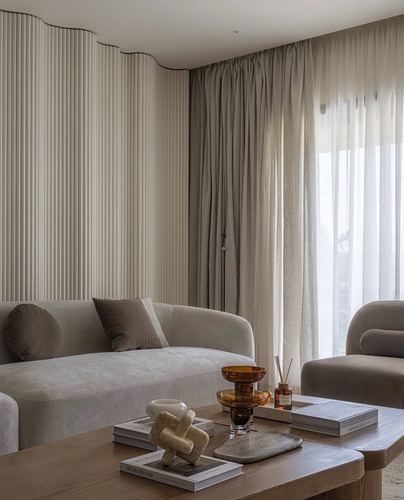 Curved beige sofa against fluted wall panelling with sheer curtains and a wood coffee table