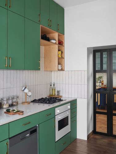Green kitchen cabinetry with brass handles, wood shelving niche, and glazed black door beyond