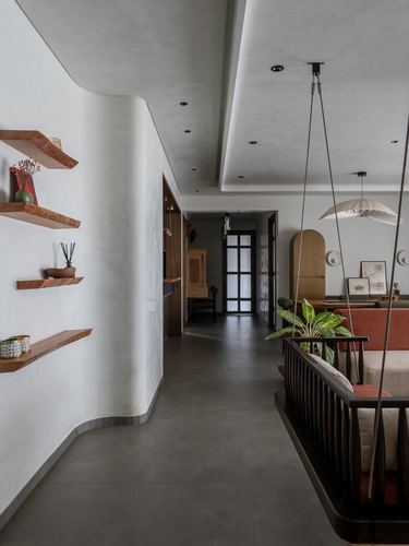 Curved white plastered corridor with wood shelves leading to a suspended wooden swing and living room