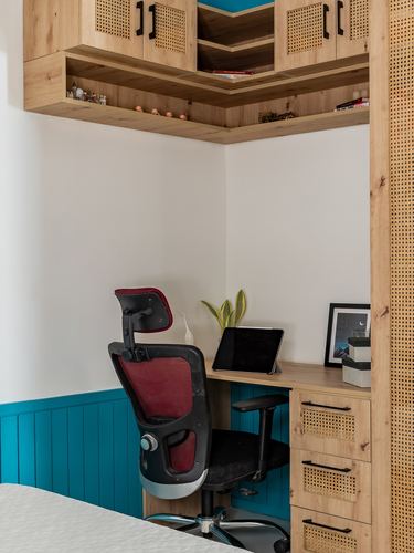 Corner study desk under cane-fronted wood cabinetry with teal wainscoting and a black office chair
