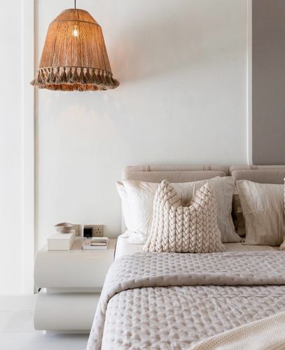 Beige bedroom corner with woven pendant light beside upholstered bed and white nightstand