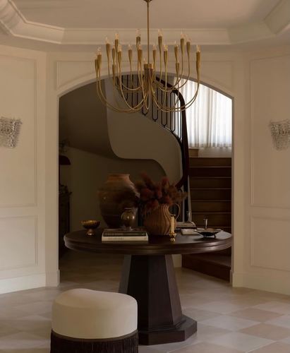 Foyer with round dark wood table, brass chandelier, and arched opening to curved staircase