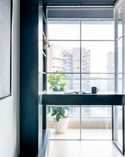 Black built-in desk beneath floor-to-ceiling window overlooking city skyline, with plant and mug