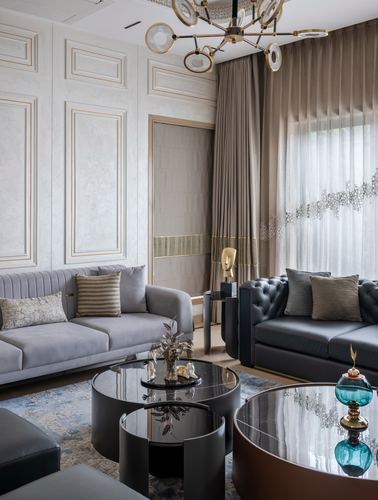 Living room with grey velvet and black leather sofas around round glass coffee tables under a sputnik chandelier