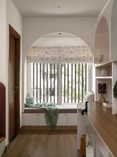 Arched window seat with floral blind, wood slats, and adjoining study desk in child's room