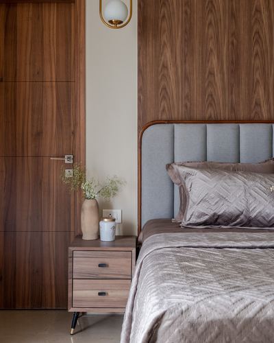 Bedroom corner with wood-panelled wall, curved upholstered headboard, and wooden nightstand with vase