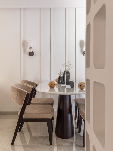 Round marble dining table with mocha velvet chairs beside a fluted paneled wall and perforated screen