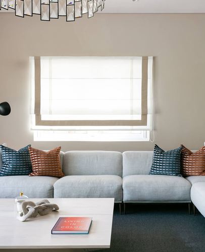 Neutral living room with grey sectional sofa, patterned throw pillows, roman blind, and marble coffee table