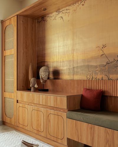 Wooden foyer cabinet with cane inlay panels beside a bench seat and a golden landscape mural wall.