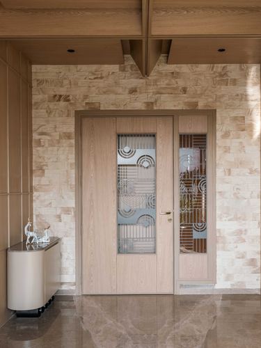 Wooden entry door with art deco glass grille beside a stone-clad foyer wall