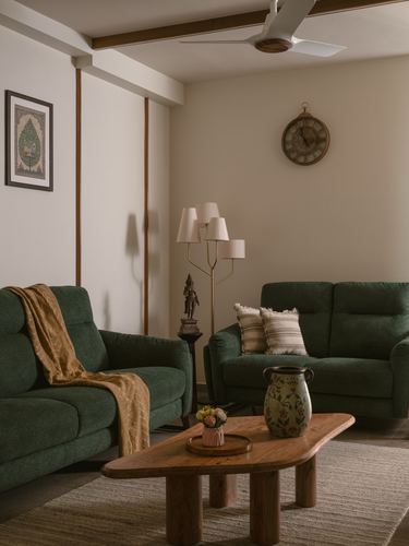 Living room with two green sofas, wooden coffee table, brass floor lamp, and wall clock