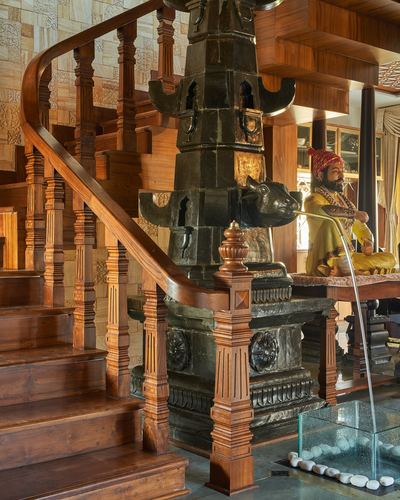 Carved teak staircase spiraling around a black stone fountain with a warrior figurine in a heritage Wada home