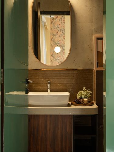 Powder room with oval brass mirror, white vessel sink, dark wood vanity, and green glass door.