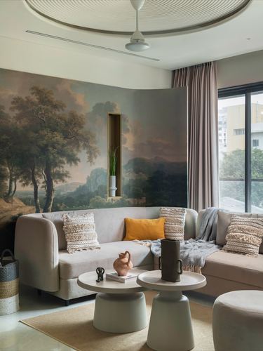 Beige curved sofa against a landscape mural wall with round coffee tables in living room