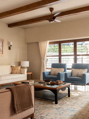 Living room with wooden beam ceiling, cream sofa, blue armchairs, and glass coffee table