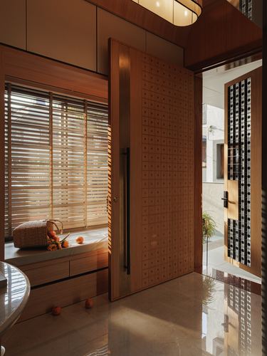 Wood-clad foyer with patterned pivot door, window seat, and slatted blinds letting in warm light