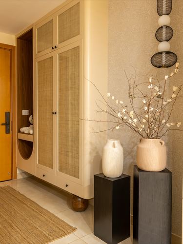 Foyer with cane-panel wardrobe, textured wallpaper, and pedestal vases holding dried branches