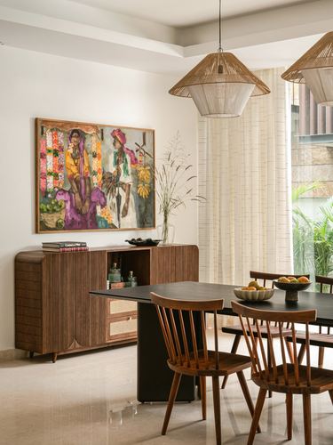 Dining room with black table, wooden windsor chairs, ribbed sideboard, painting, and woven pendant lights
