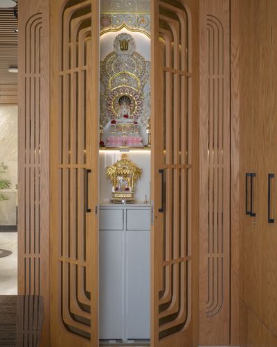Fluted wood pivot doors open to reveal a gold-backed mandir niche