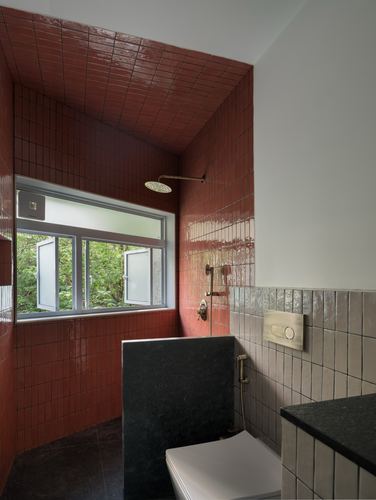 Bathroom with red glazed tile shower alcove, black stone partition, and window overlooking greenery
