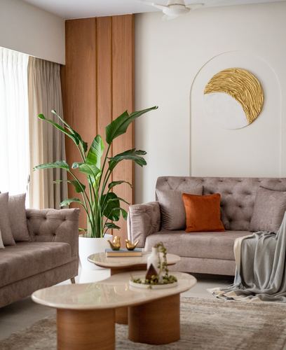 Beige tufted sofas around oval marble-topped coffee tables beneath an arched gold wall art