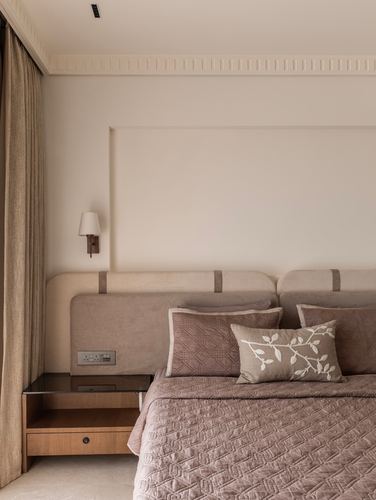 Beige and dusty pink bedroom corner with upholstered headboard, wall sconce, and wooden bedside table