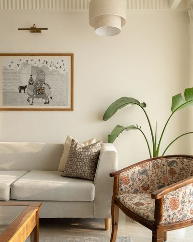 Beige living room corner with sofa, folk art print, floral armchair, and banana leaf plant