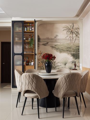 Round dining table with quilted beige chairs beneath a tropical mural wall and open bar cabinet