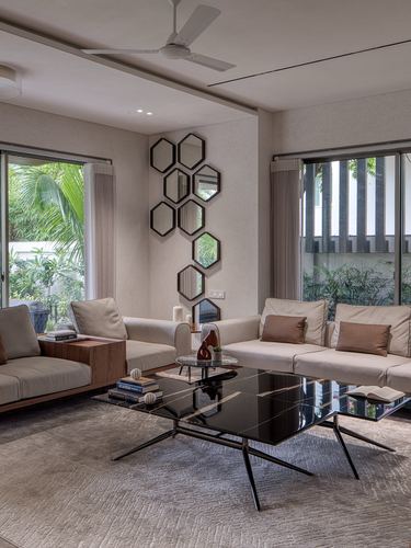 Neutral living room with L-shaped sofa, black glass coffee table, and hexagonal mirror arrangement on wall