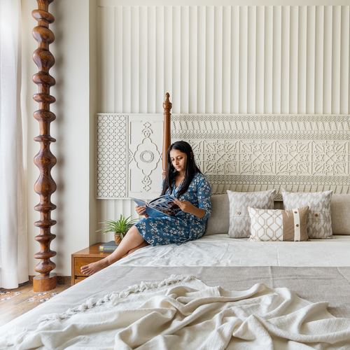 Woman reading on a bed with a carved wooden post and textured plaster headboard wall