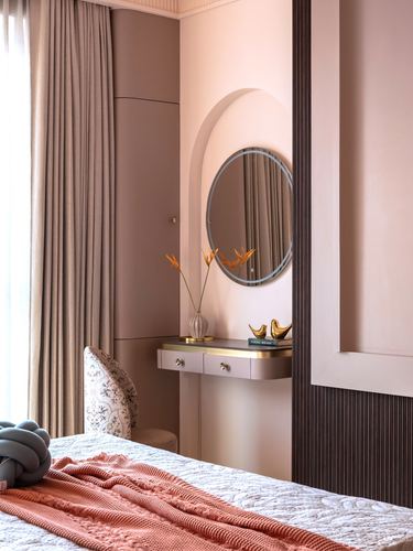 Blush pink bedroom corner with arched mirror above dressing table and terracotta throw on bed