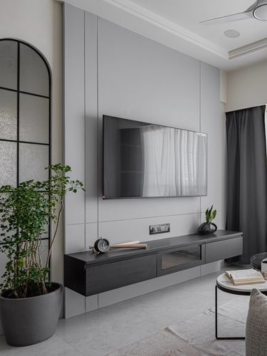 Grey panelled tv wall with floating black console, arched mirror and potted plant in minimalist living room