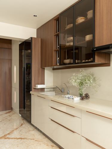 Galley kitchen with walnut cabinetry, glass display shelves, and cream marble countertop and flooring