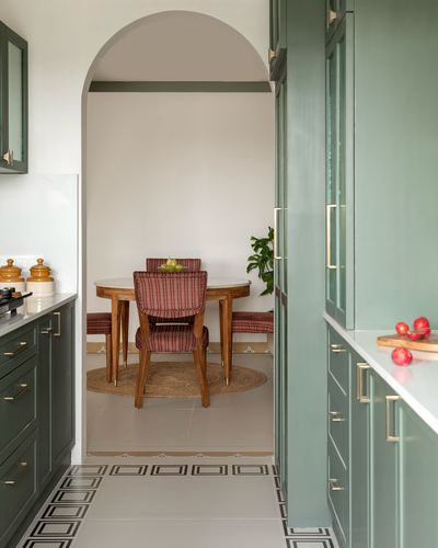 Green kitchen cabinetry frames an arched doorway opening to a small patterned dining nook.