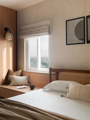 Sunlit bedroom with cane headboard, wood window seat, and framed abstract art