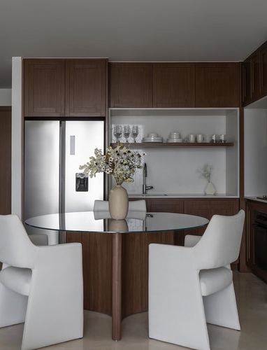 Dark wood kitchen with glass dining table, white chairs, and open shelving displaying glassware and ceramics
